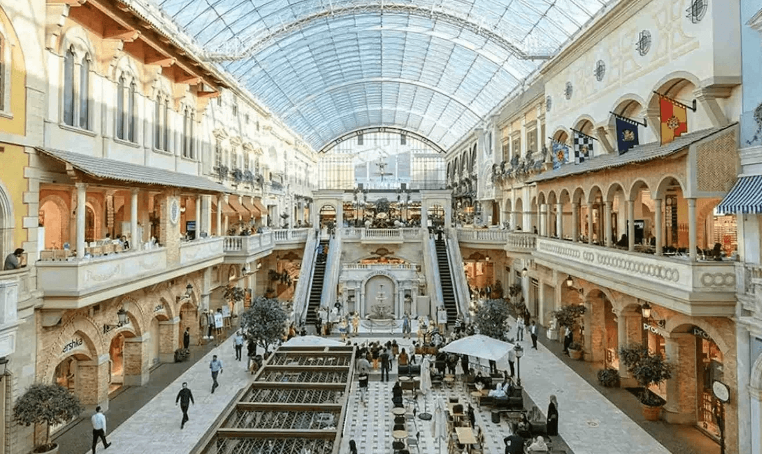 Mercato Shopping Mall with a high glass roof, European-style architecture, escalators, and multiple retail and dining areas.