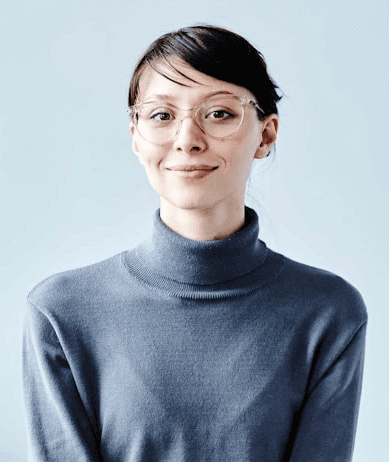 Smiling young man with short hair poses against a dark background, wearing a green button-up shirt.