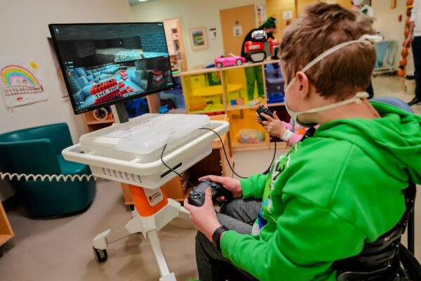 Two kids play Minecraft on a GO Kart, featuring a Lenovo Legion monitor, in the children's playroom of a hospital.