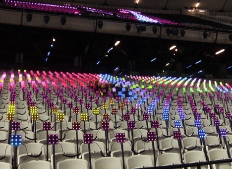 Colorful LED lights illuminate rows of stadium seats, creating a vibrant display of red, blue, green, and yellow lights in a pattern across the seating area.