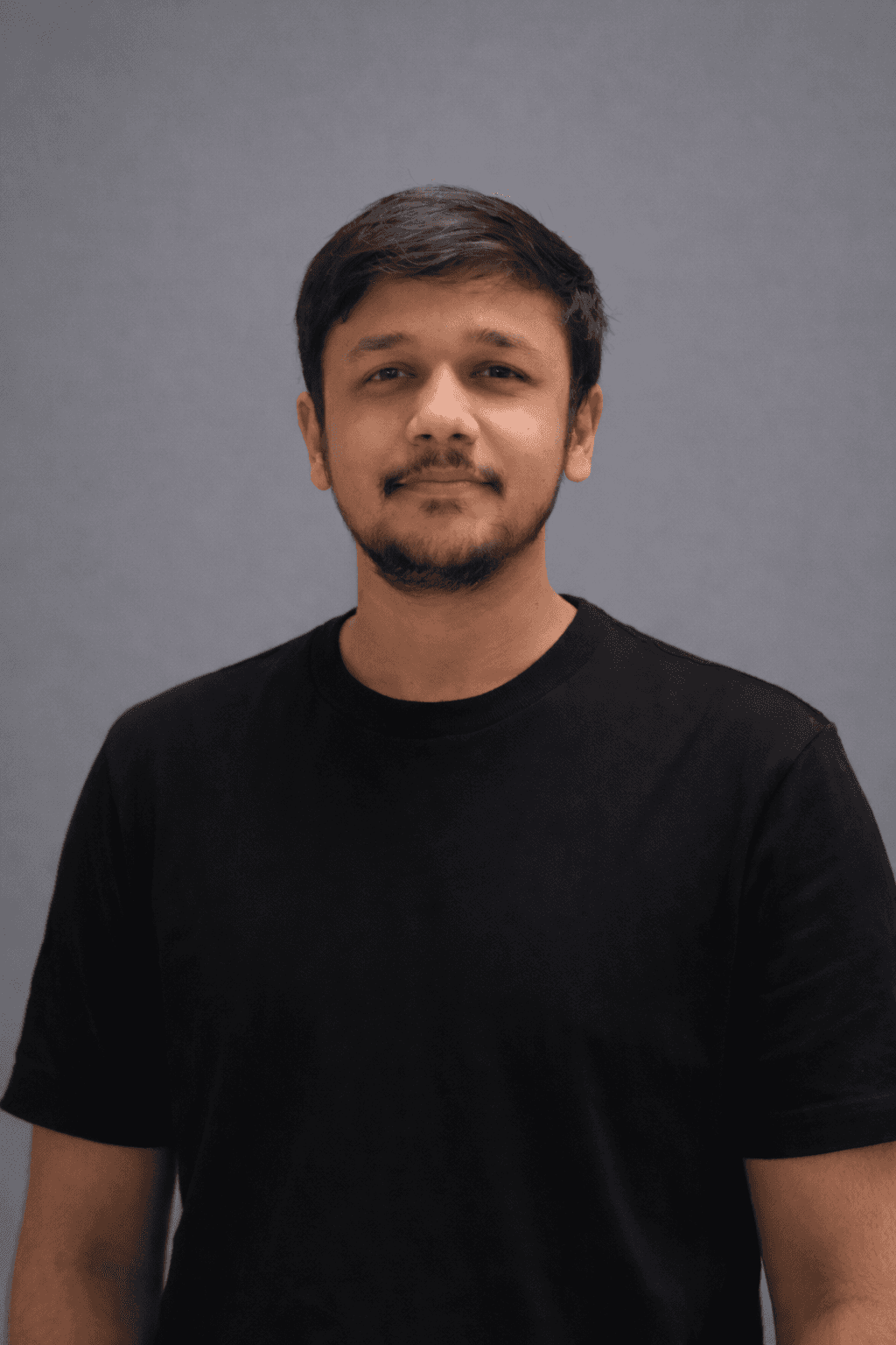A young man with short hair wearing a white shirt, smiling and looking directly at the camera.