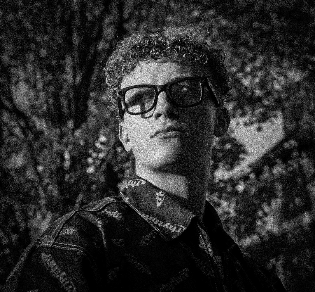 A thoughtful young person with dark hair gazes to the side, captured in soft black and white lighting.