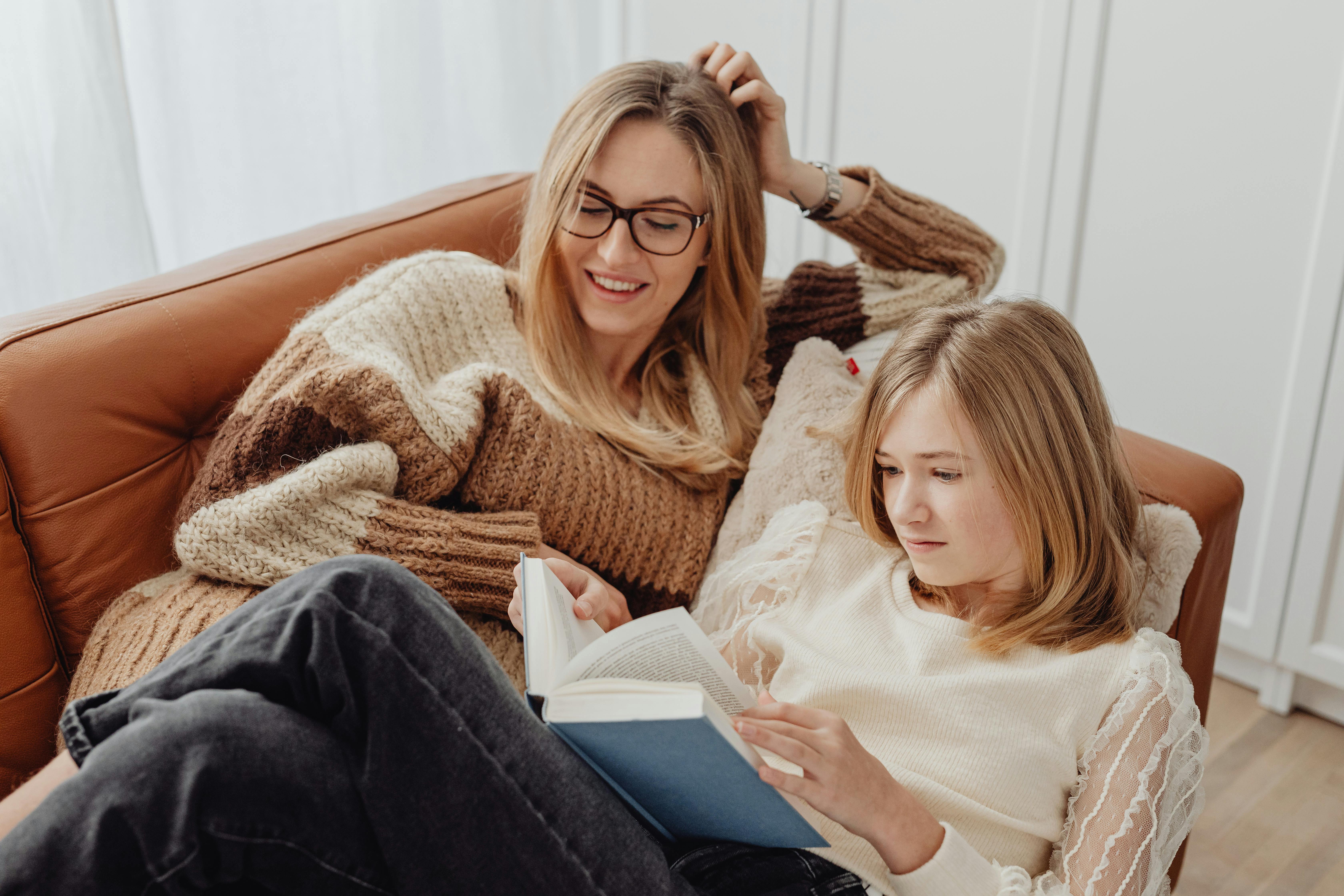 Conversion Truth for Families - Mother in sweater lounging on couch with her teenaged daughter, reading a book together