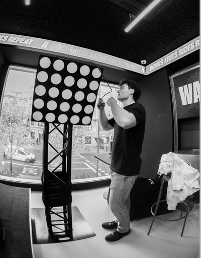 A smiling man with short hair stands with arms crossed, wearing a dark shirt against a neutral background.
