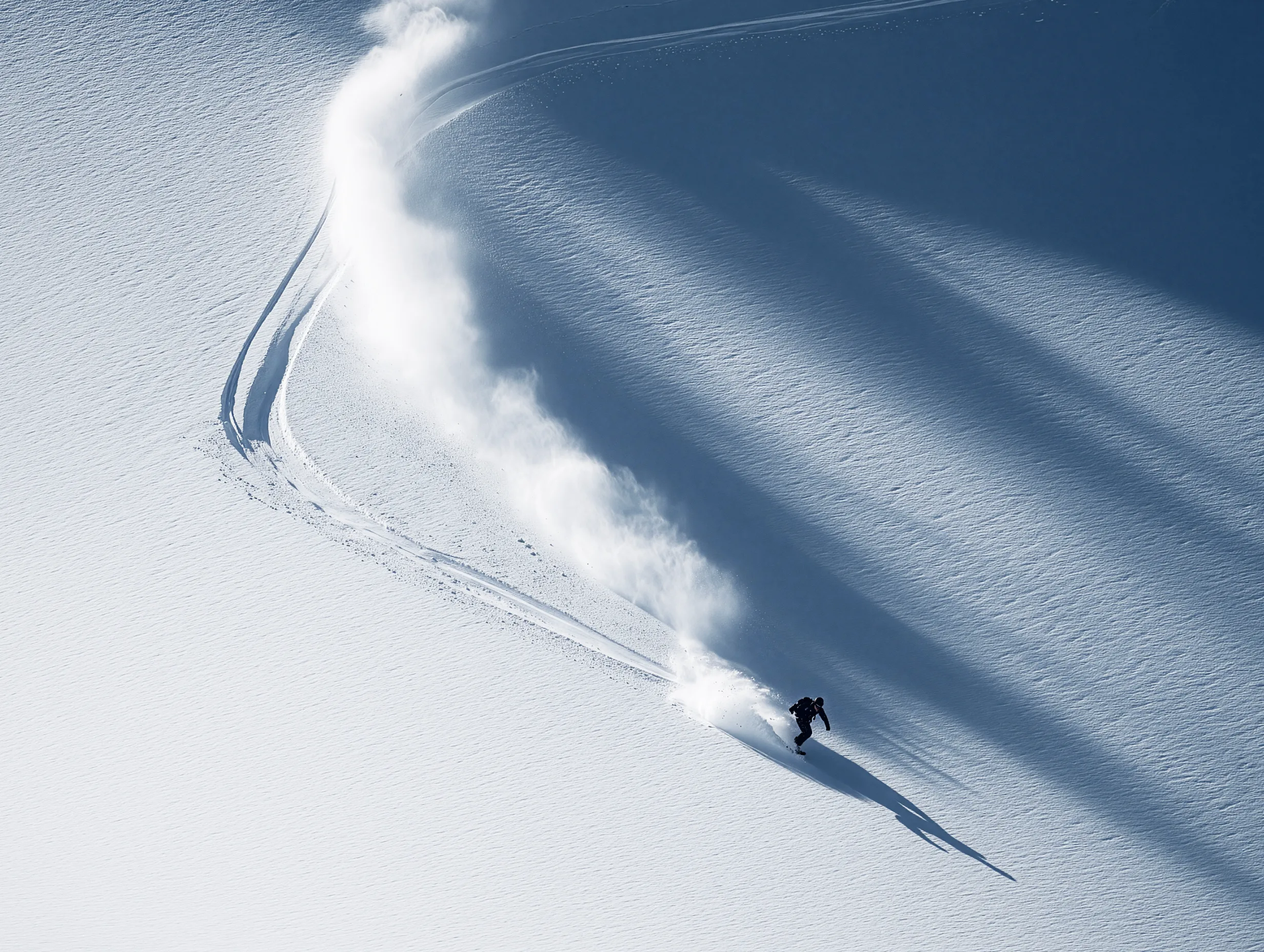 Aerial view of a snowboarder descending a wide snow-covered slope leaving a trail behind