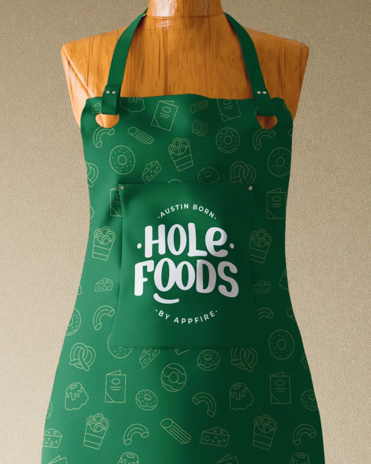 A green apron with "Austin Born, Hole Foods by Appfire" printed in white over a white shirt. The apron pocket has a playful food icon pattern.