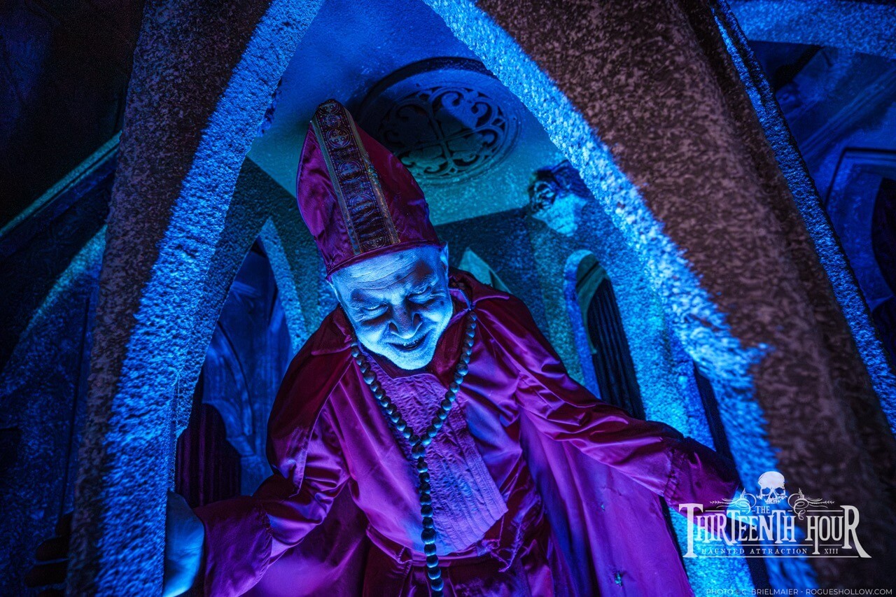 Sinister bishop-like scare actor in blue-lit stone arches