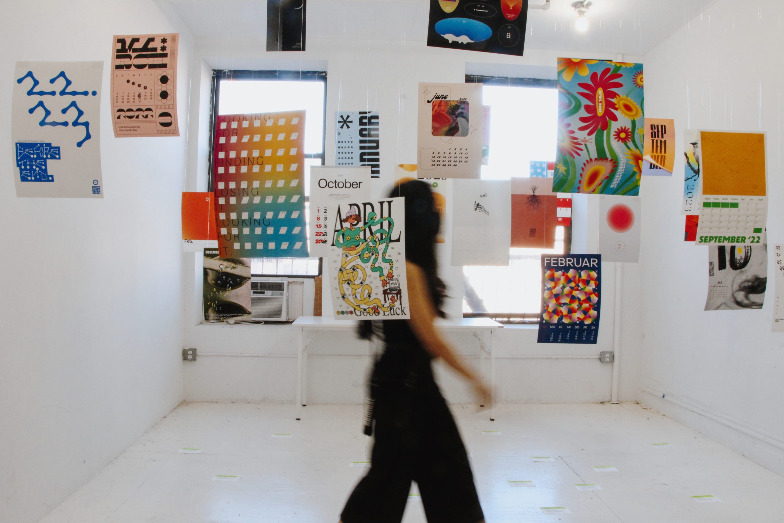 Exhibition with multiple multi-colored posters hanging from the ceiling and e person crossing the room