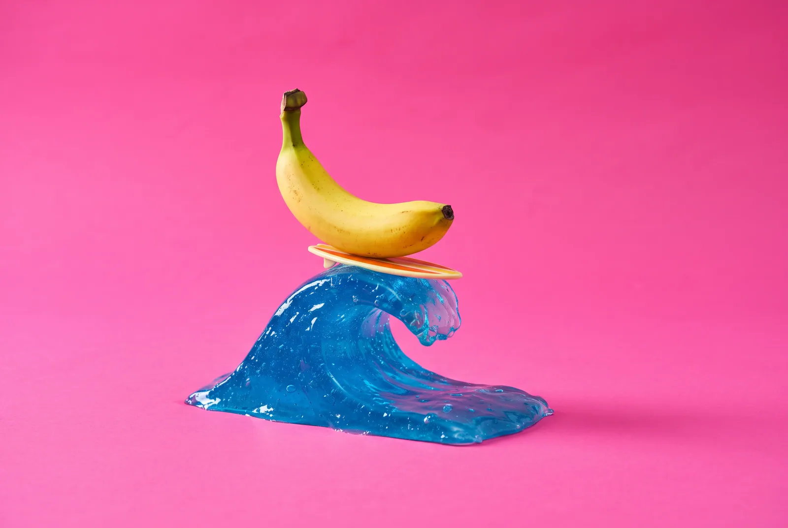 A banana riding a tiny surfboard on a glossy blue wave, a playful image for urge surfing