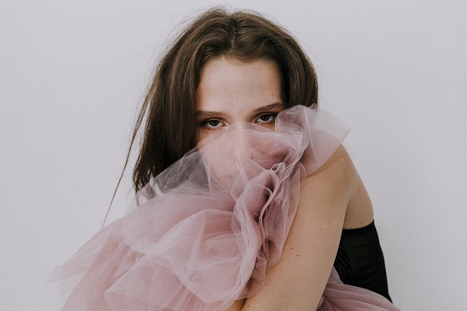 A model with her face partially covered in pink tulle, highlighting a soft, feminine aesthetic during a 90s vintage photoshoot at Revelator Studio, Shreveport.