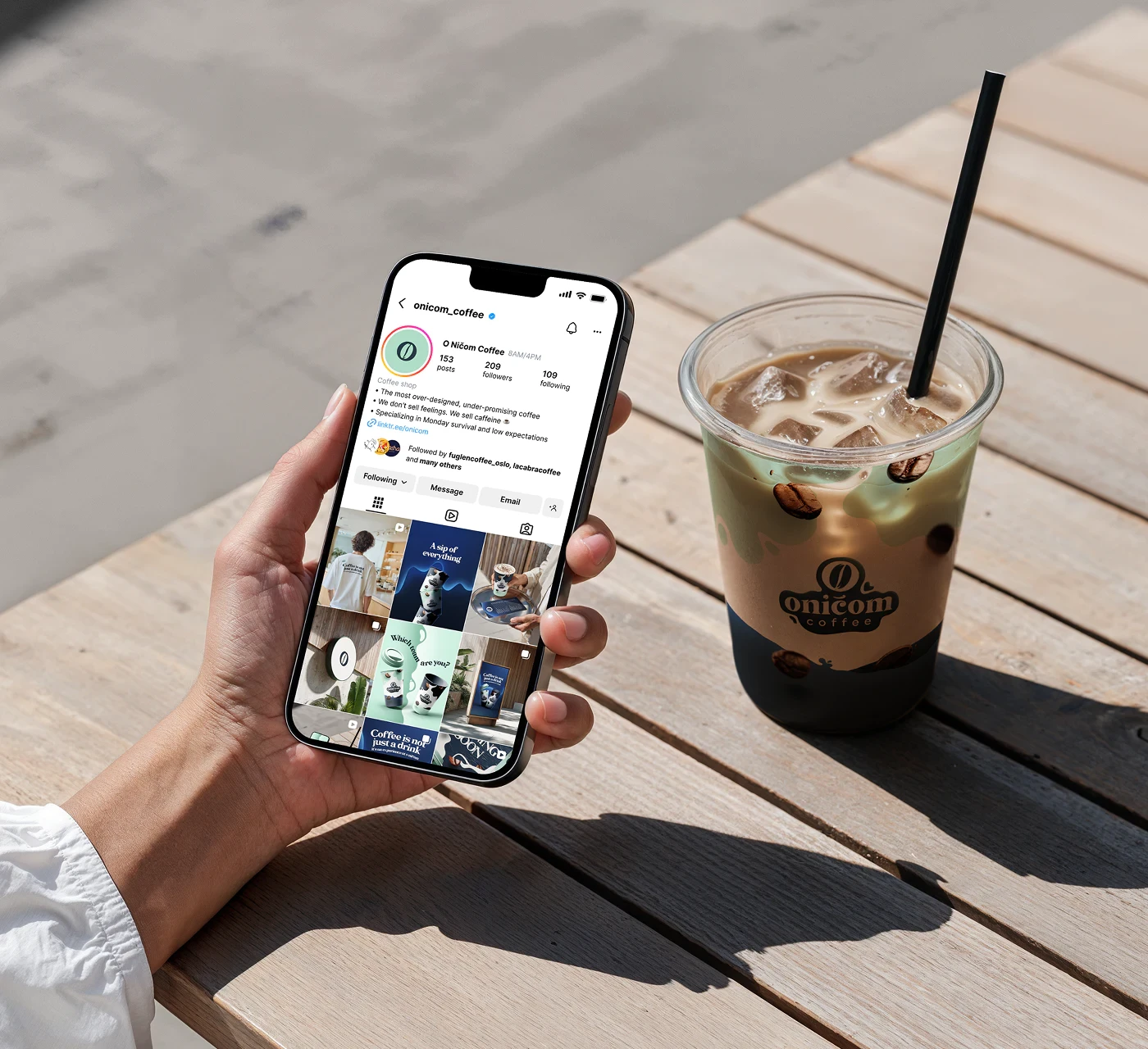 Hand holding a smartphone showing O Ničom mobile app next to iced coffee.