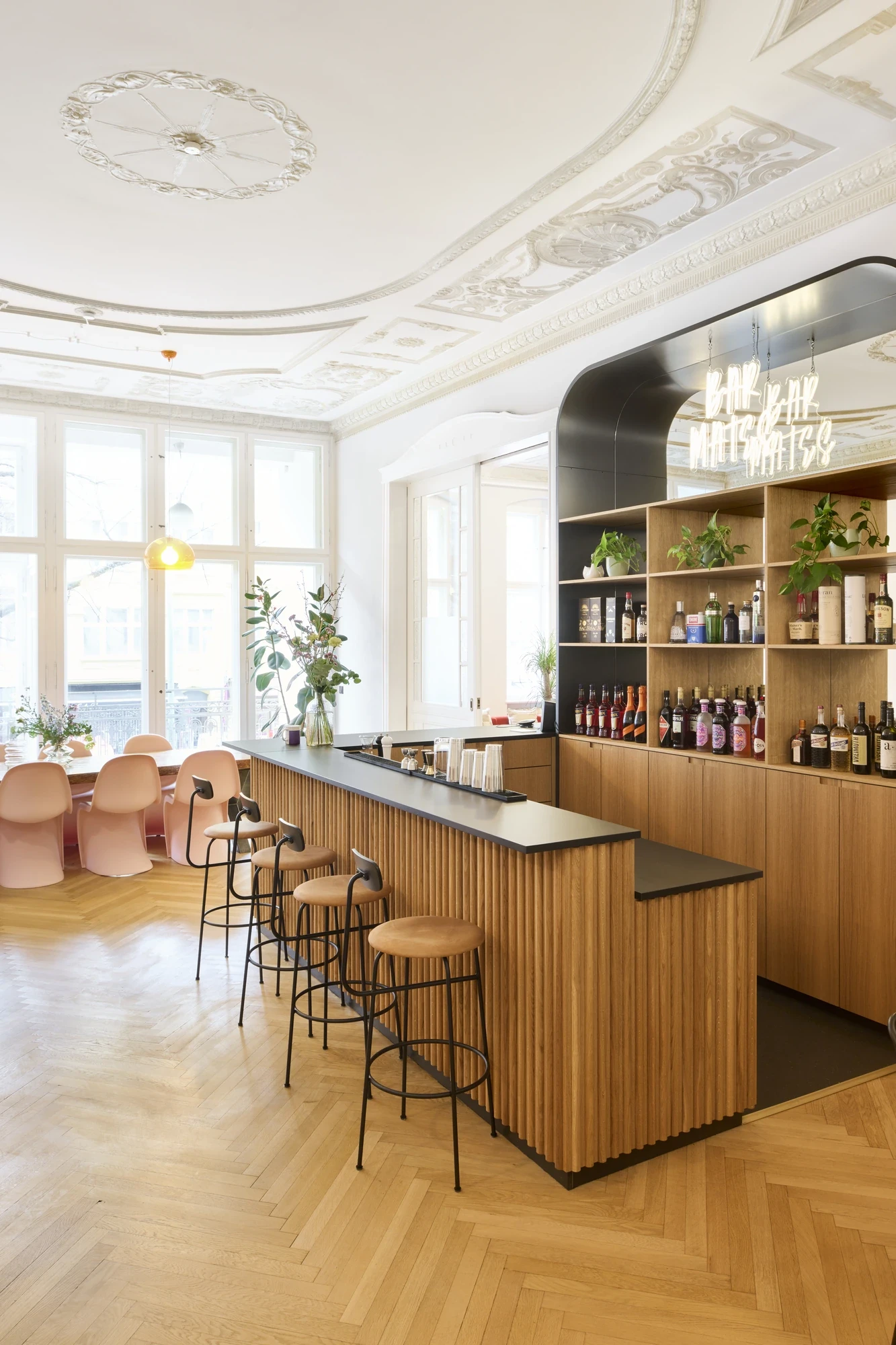 In-house office bar with fluted wooden counter, stools and a black mirror backbar in a classic Altbau room with stuccoed ceiling and parquet floor.