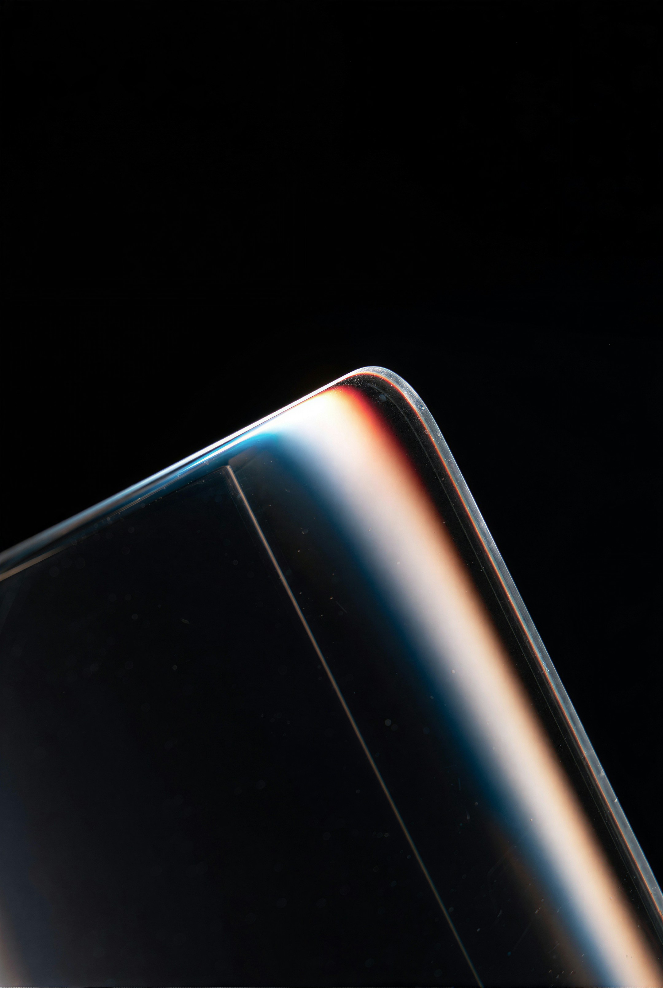 Close-up of a curved glass edge with colorful light reflections.