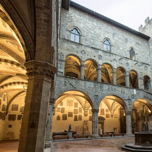 Cour historique aux arches en pierre et aux sculptures décoratives, entourée d’un bâtiment de plusieurs étages aux fenêtres cintrées.