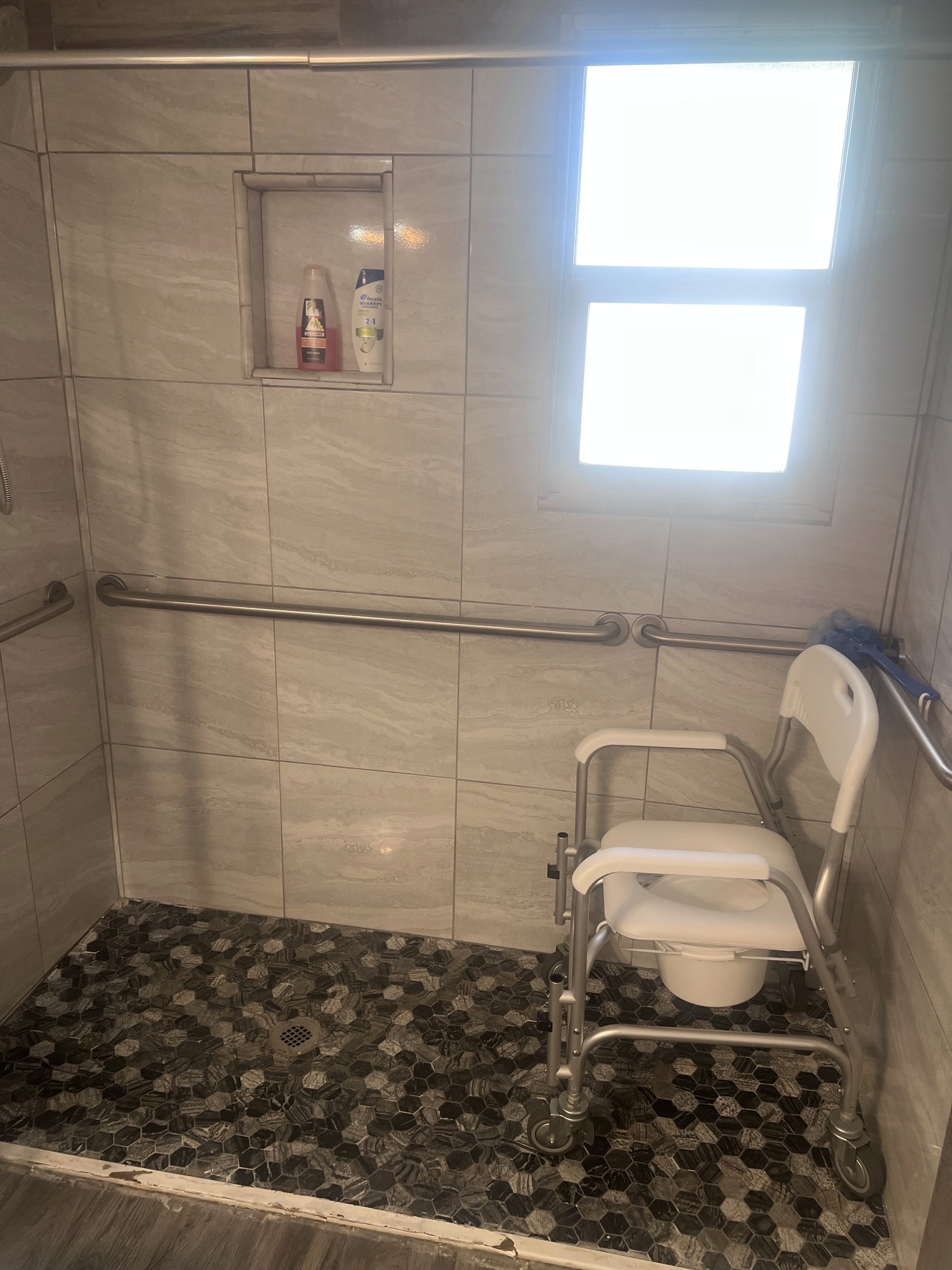 Curbless shower entry with a rolling shower chair and wall grab bars