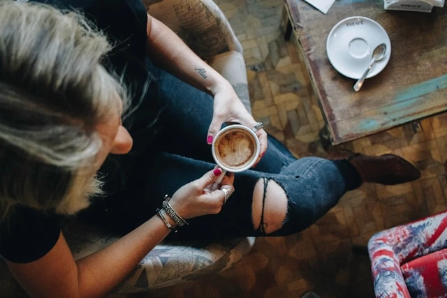 Person sitting with a cup of coffee at a wooden table, creating a calm weekday morning routine.