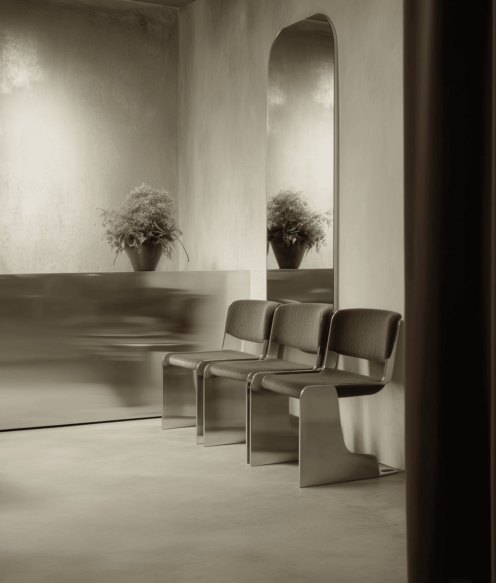 Minimalist interior with sleek metallic chairs, an arched mirror, and soft lighting. A potted plant adds a touch of nature to the modern design.