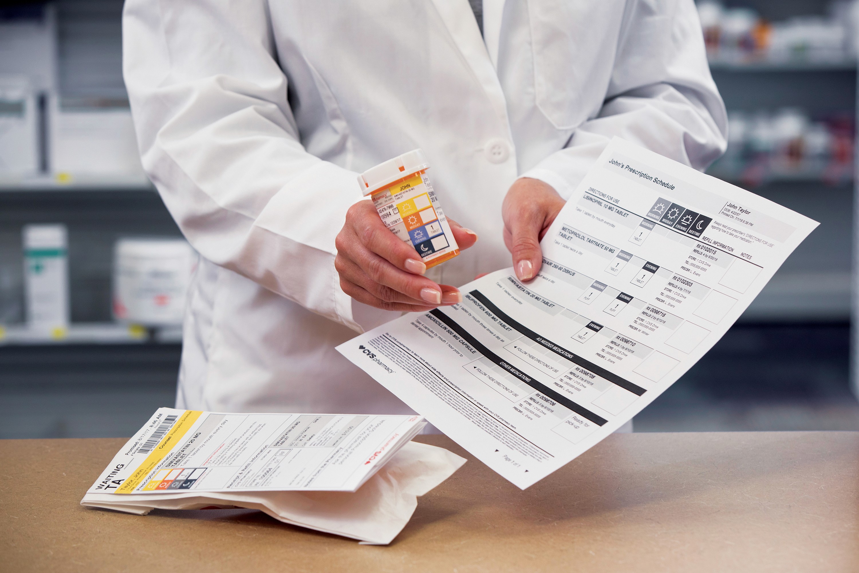 A photo of a pharmacist showing a labeled pill bottle and some prescriptions.