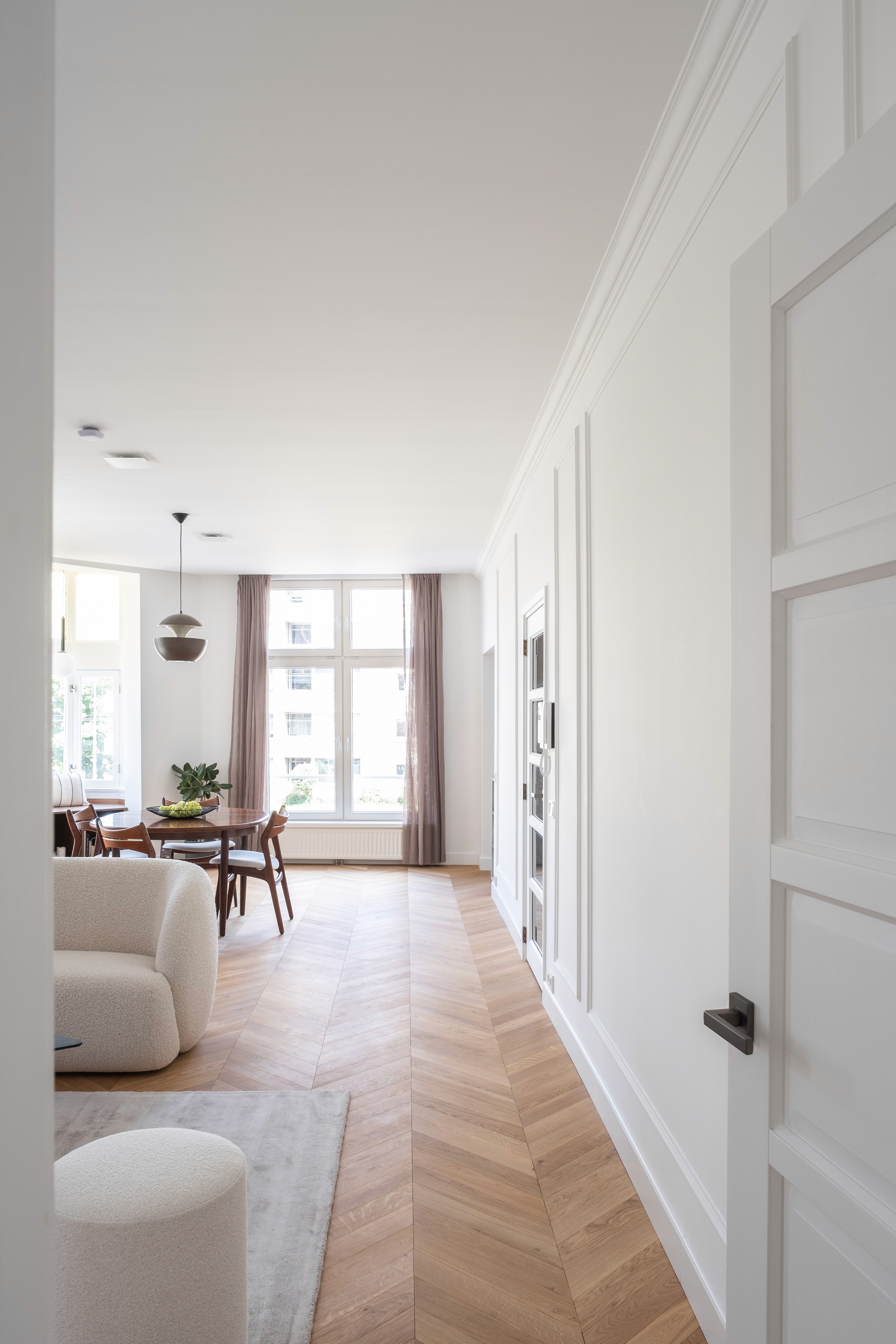 Open-plan living and dining area with white Parisian-style panelled doors and mouldings, Hungarian Point parquet, white bouclé sofa, and mid-century dining set