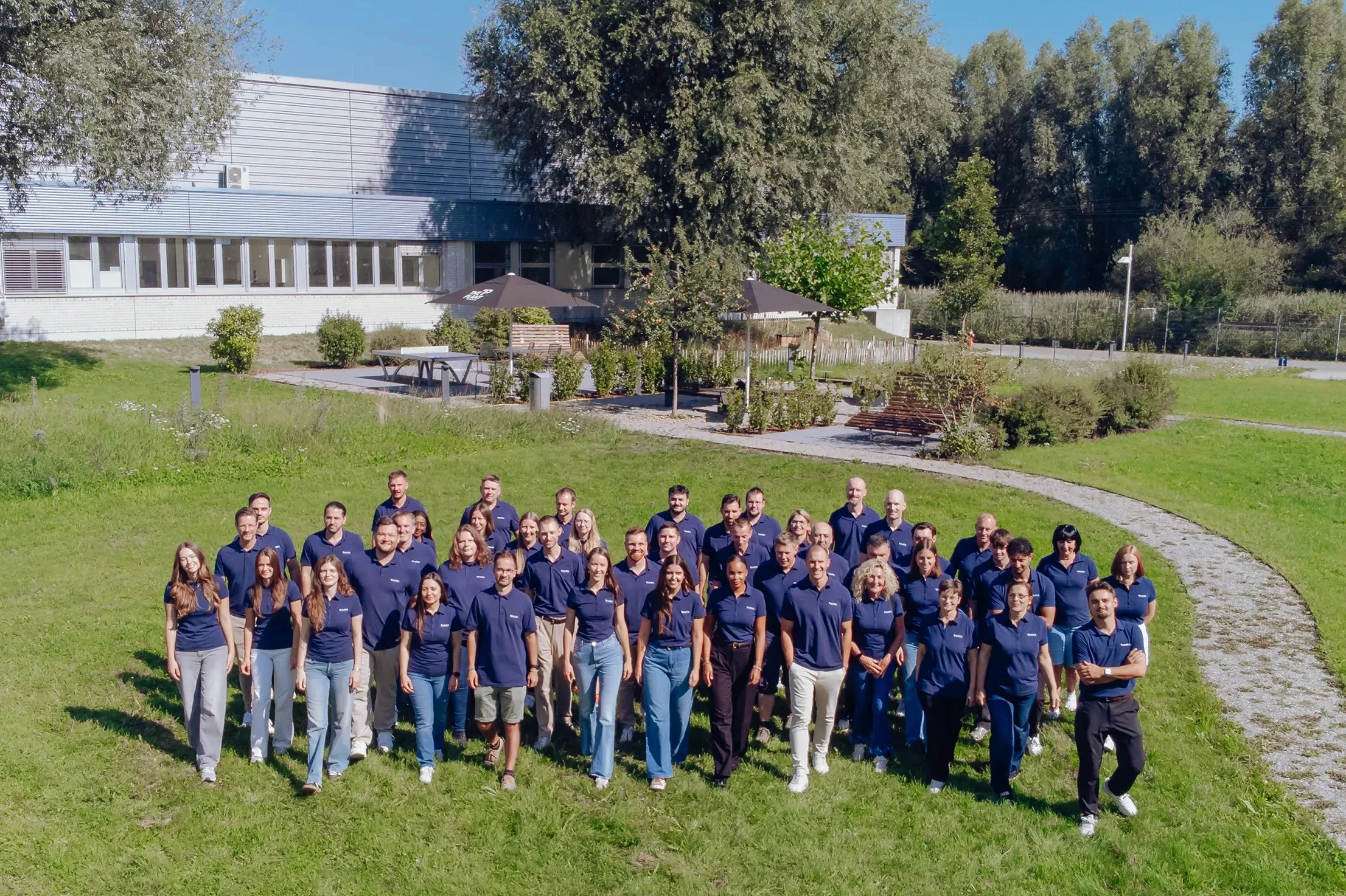 A large group photograph of the Bedifol workforce wearing dark blue polo shirts, taken on a lawn in front of the company building.