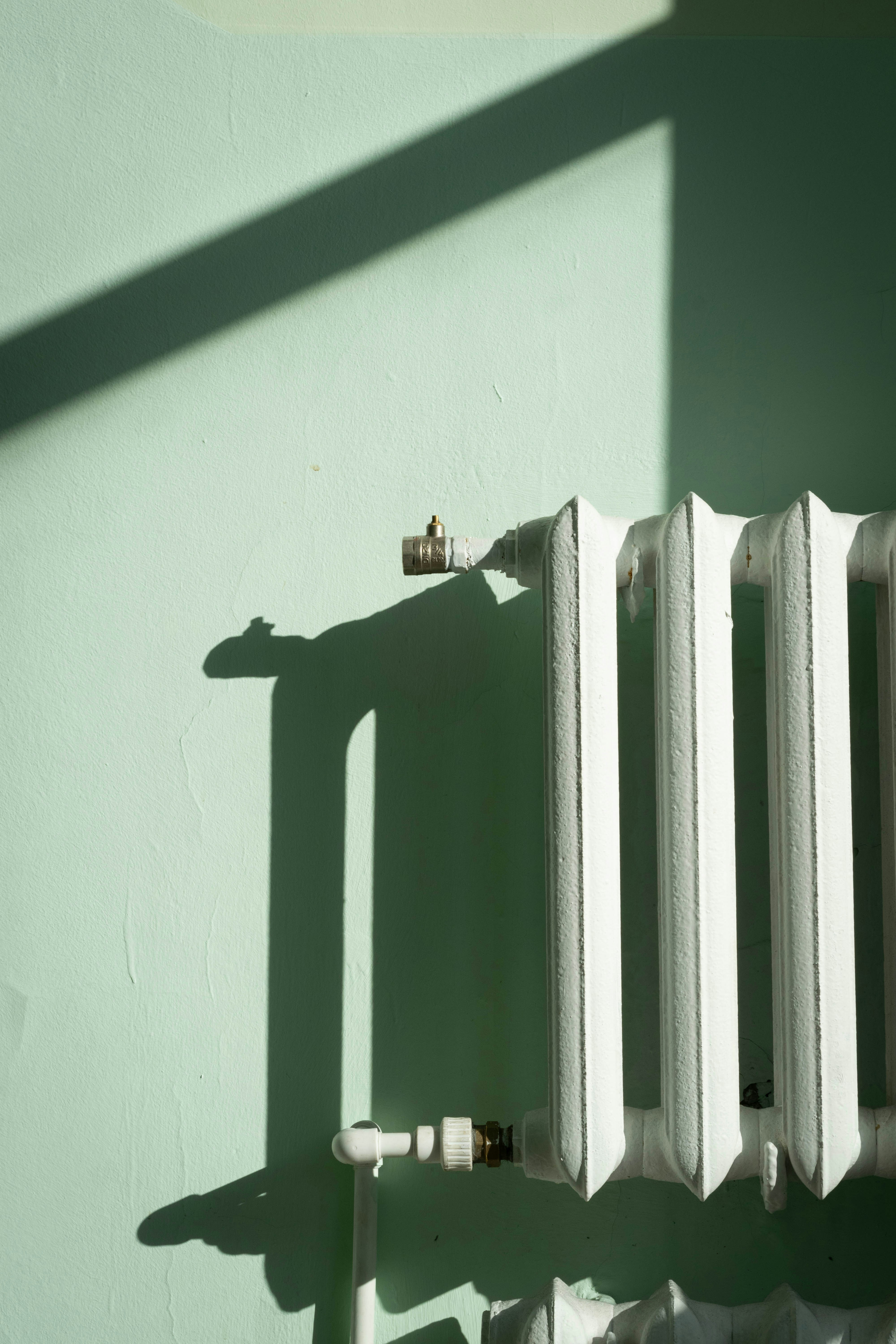 White radiator against a pale green wall with shadows.
