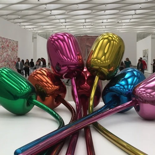 A colorful metallic tulip sculpture in a modern art gallery with people viewing various artworks in the background.