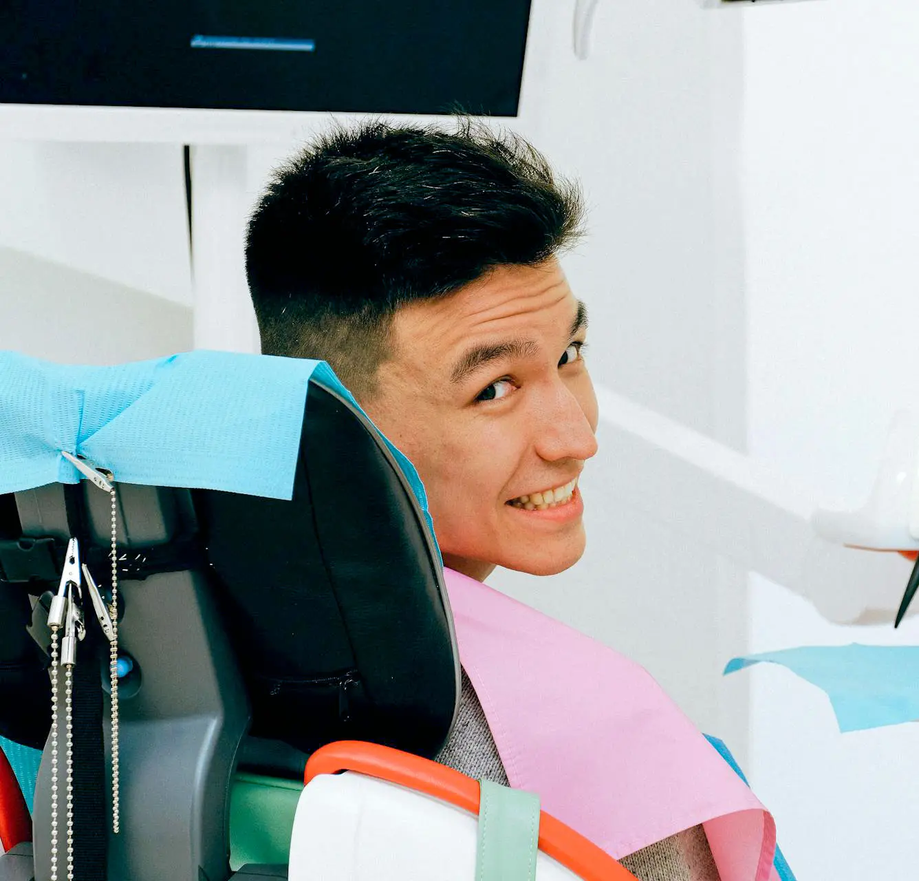 Young man smiling in a dental chair with blue and pink bibs