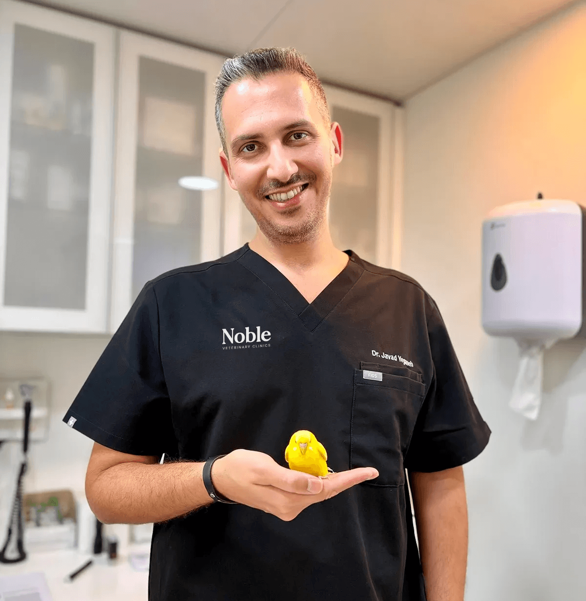 Dr. J. Yeganeh, avian veterinarian at Noble Veterinary Clinics Dubai, gently holding a pet bird during a wellness checkup