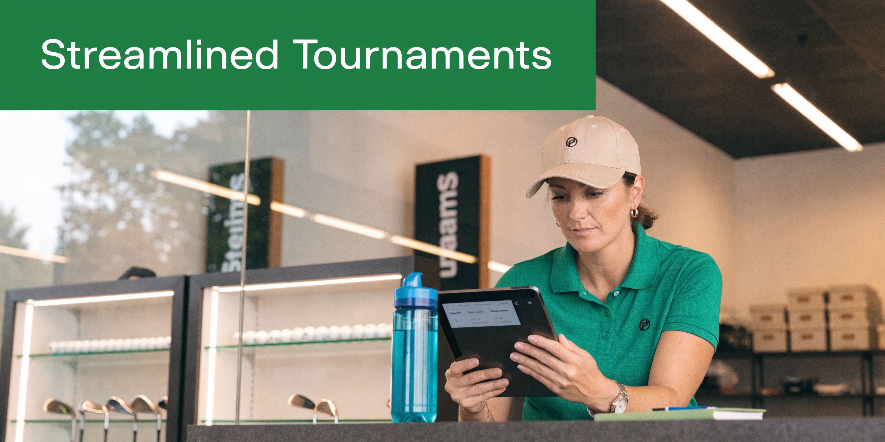A woman in a green golf shirt works on a tablet at a golf course clubhouse counter.