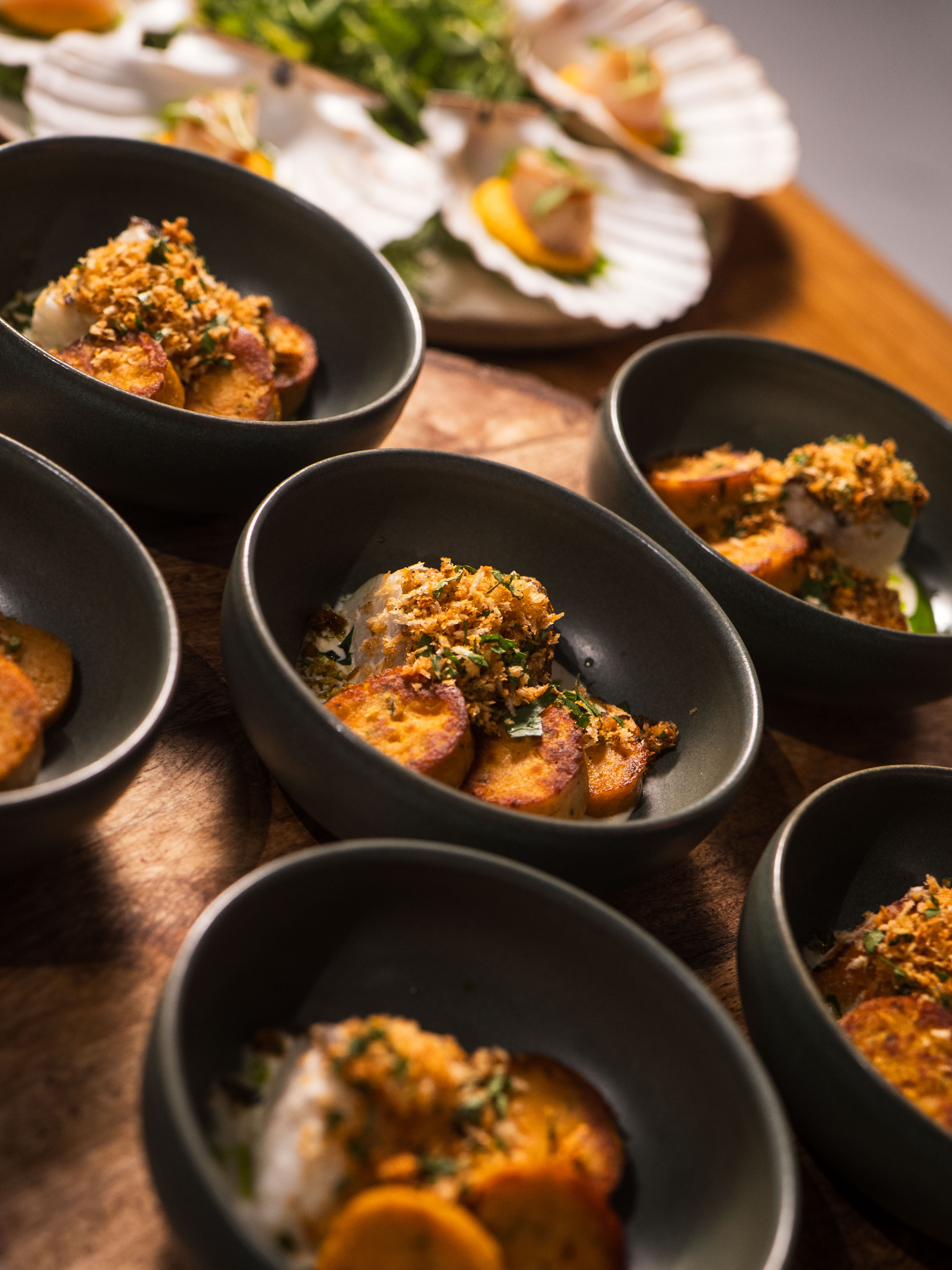 A top-down view of several black bowls filled with various dishes, accompanied by leafy greens on the side.
