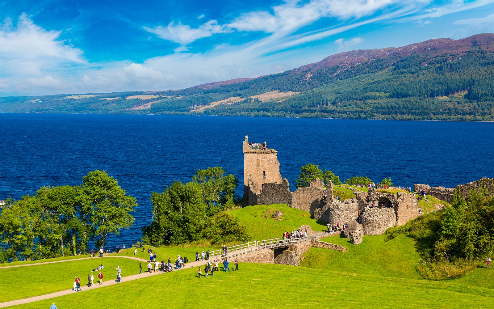 Urquhart Castle ruins overlooking Loch Ness with visitors exploring the grounds.