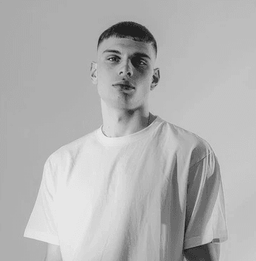 A young man in a white t-shirt stands against a light-colored background.