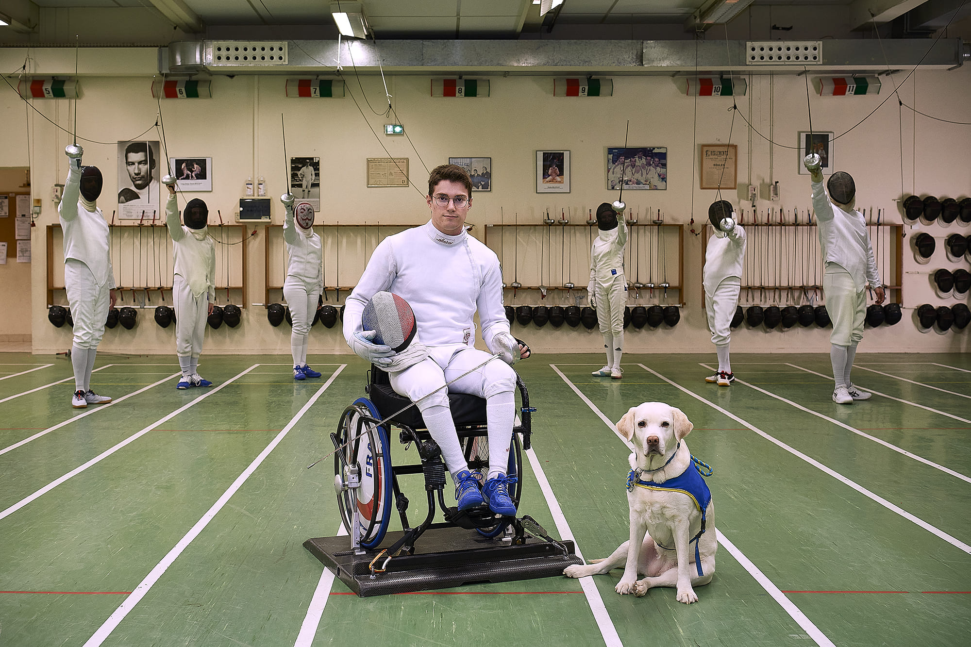 Quentin accompagné de son chien d’assistance Junon, photographiés par Frédéric Bourcier lors d’un entraînement d’escrime fauteuil à la Salle d’Armes du Masque de Fer, dans le cadre d’un reportage documentaire social pour Handi’Chiens.
