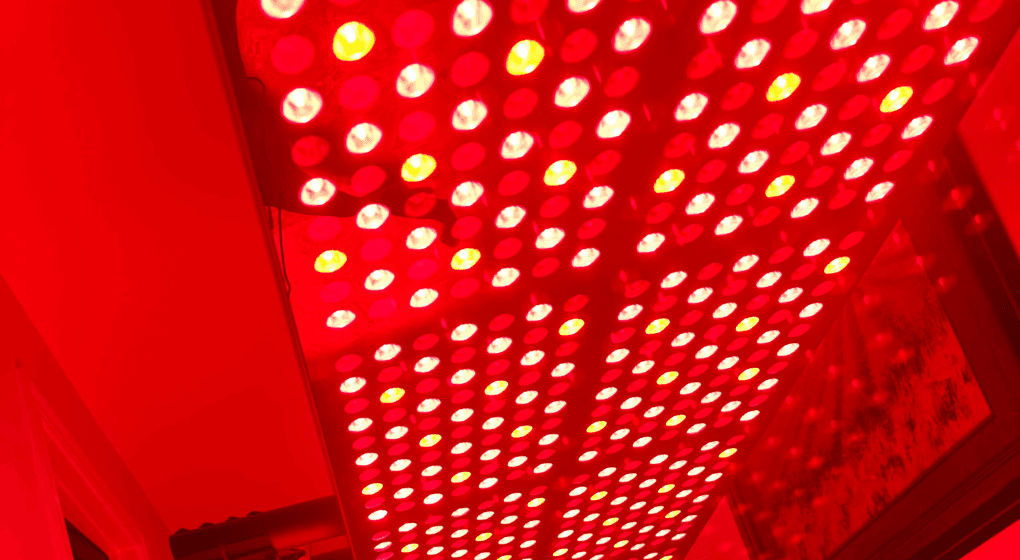 Image of a red and infrared lght therapy panel turned on with a red background