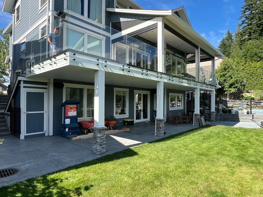 Modern two-storey home with professionally installed glass railings on the upper deck, featuring clear panels, white posts, and covered outdoor living space.