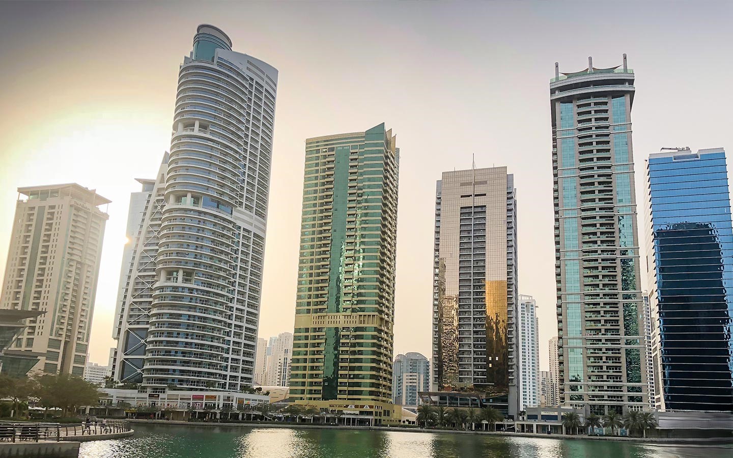 Skyline of Jumeirah Lake Towers with modern high-rise buildings reflecting over the waterfront at sunset.