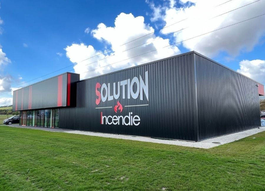 Bâtiment professionnel à bardage métallique rouge et noir sous un ciel bleu.