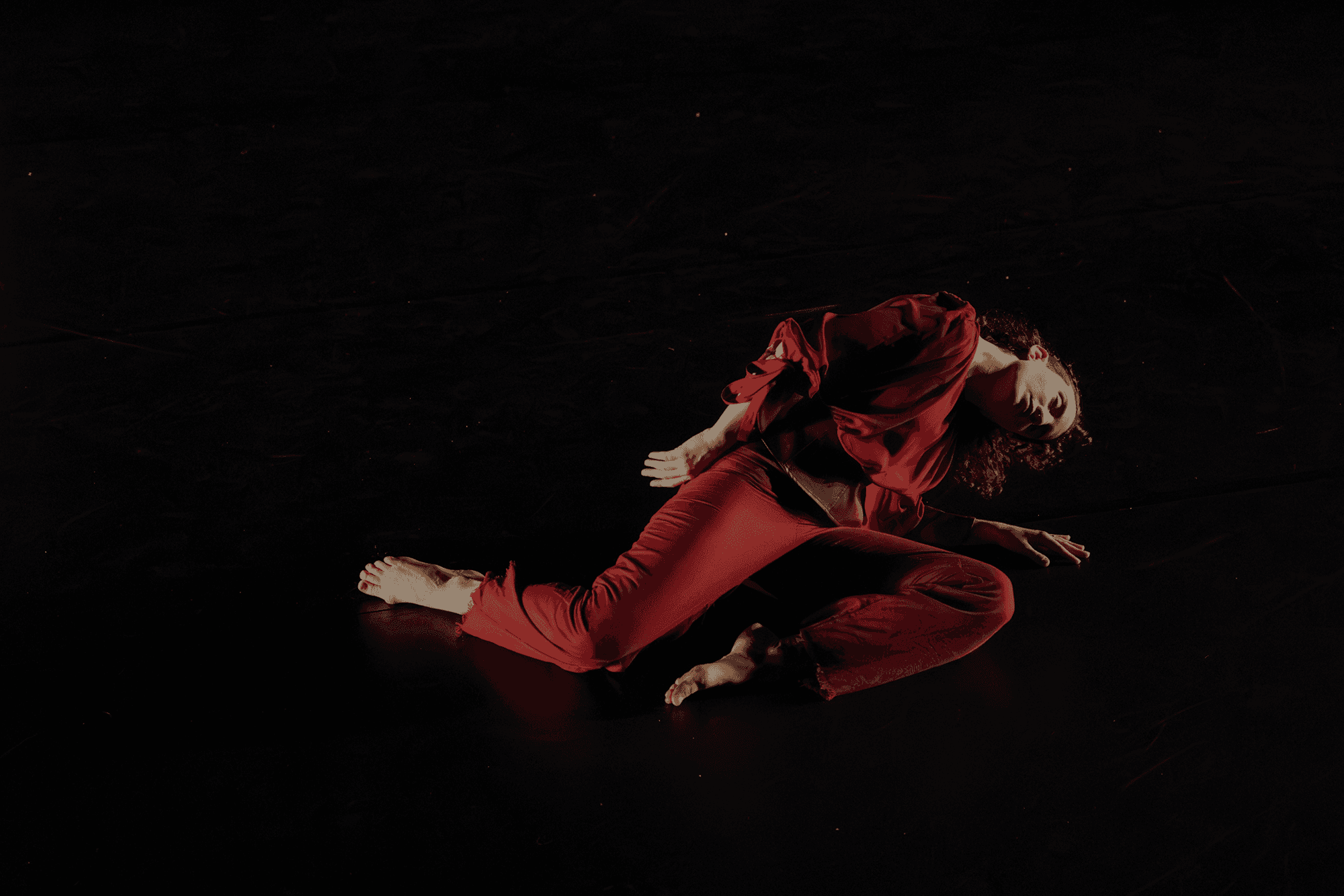 Dancer Sarah McCullough in a deep red outfit performing a dramatic back bend on a dark stage. Choreography by Julia Antinozzi, photo by Bill Cameron.