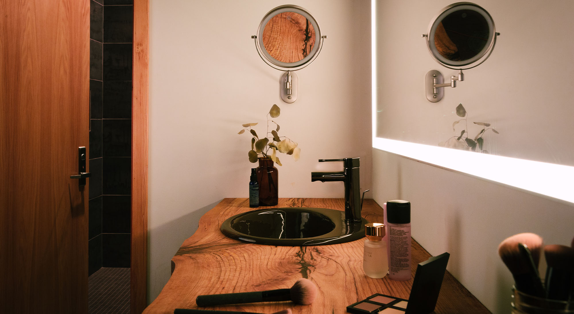 The hair and makeup counter in the greenroom at Particle Studios in Seattle. There are make-up brushes and palletes spread around next to the sink that is inlaid into a live edge counter top.
