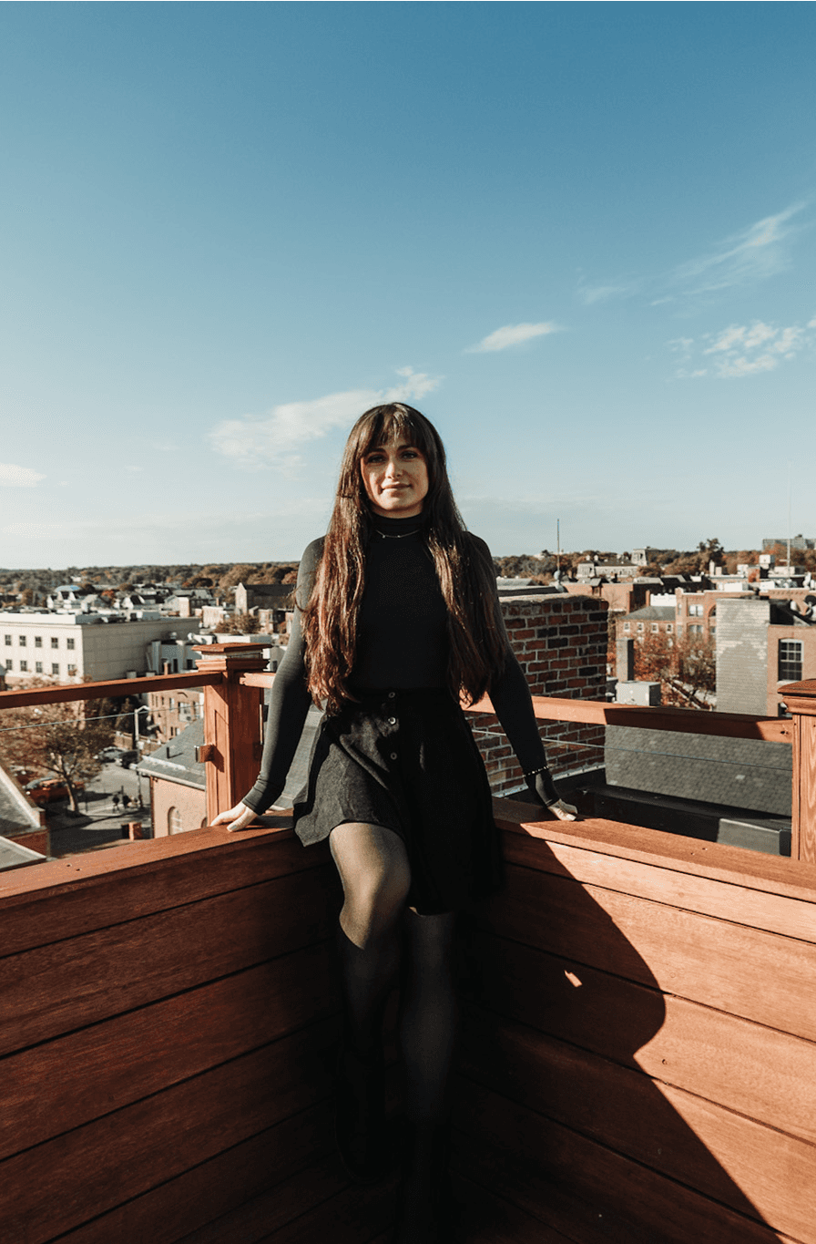 Young woman in a white shirt with a colorful gradient print, against a plain background.