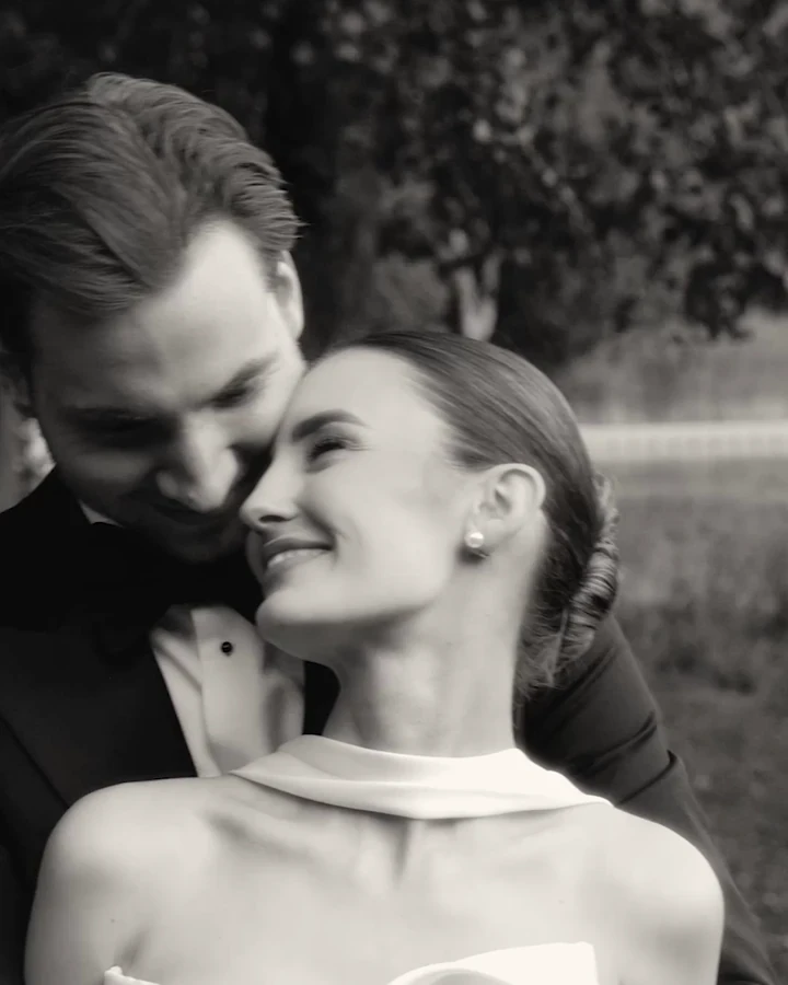 Black-and-white photo of a groom in a tuxedo leaning in to his smiling bride outdoors