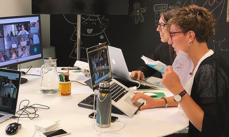 Due persone del team Triplesense Reply con laptop, monitor, appunti e schizzi sul tavolo durante una call di co-design operativo con i docenti.