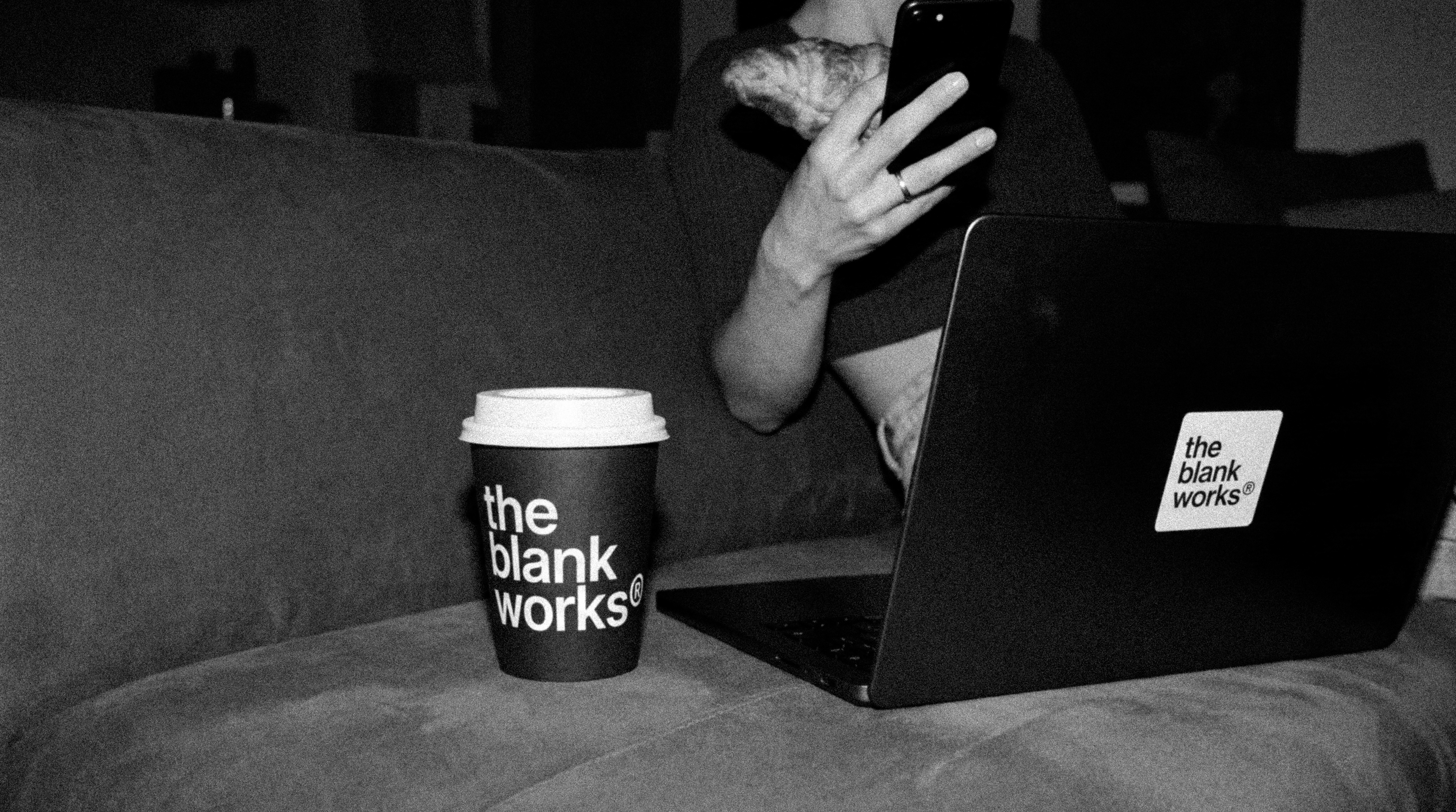Black and white image of people working at a table with laptops, showing hands gesturing during discussion of digital content displayed on screens, with fabrica® logo in the corner.