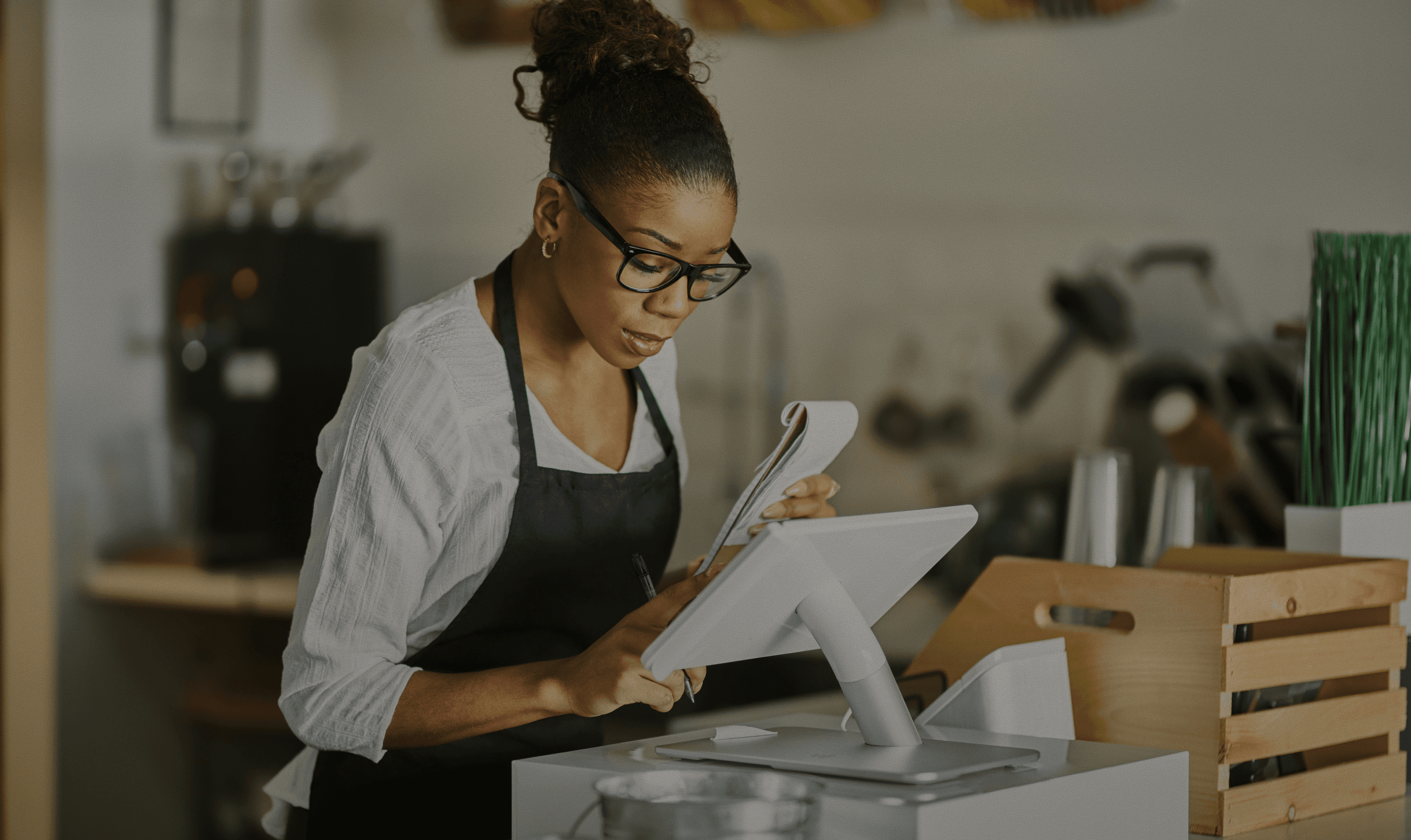 A woman stands at a digital point-of-sale system, reviewing documents, highlighting partner onboarding efficiency.