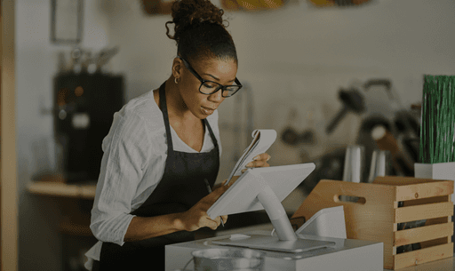 A woman stands at a digital point-of-sale system, reviewing documents, highlighting partner onboarding efficiency.