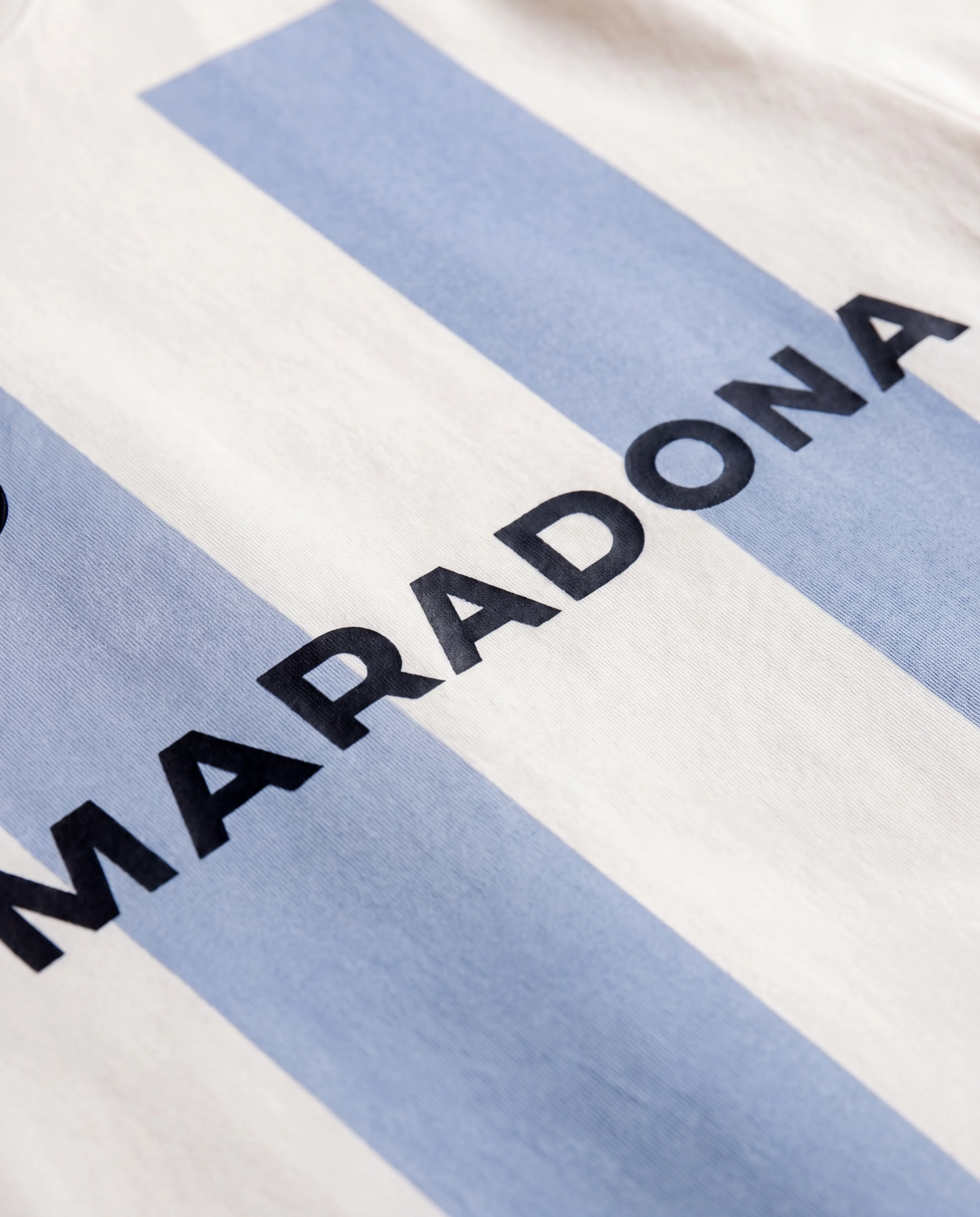 Close-up detail of the Maradona Official t-shirt fabric, showing the blue stripe pattern and MARADONA wordmark embroidered across the chest