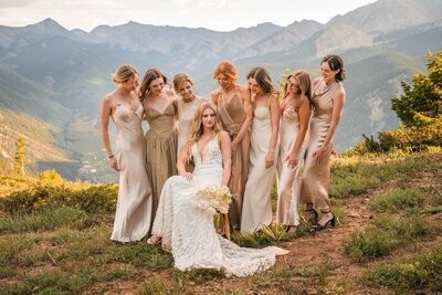 The bride sits with her bouquet, surrounded by bridesmaids in pale dresses at the mountain overlook.