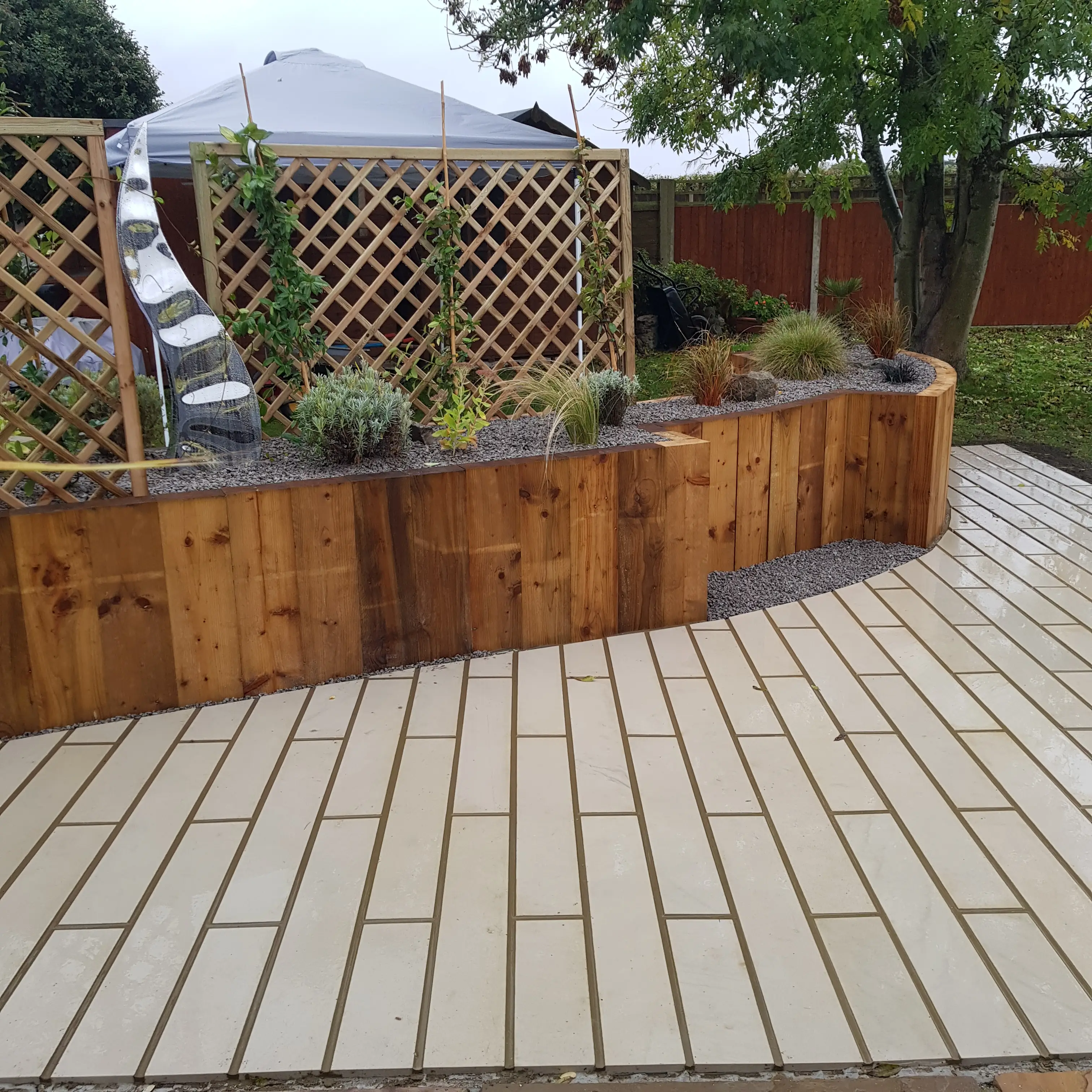 A landscaped garden area featuring wooden borders, plants, and a paved path curving around the space.