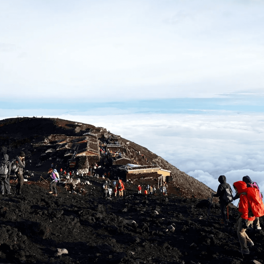 A wide shot of the sumit of Mt. Fuji with brightly-clad people in the forground and in the mid-ground