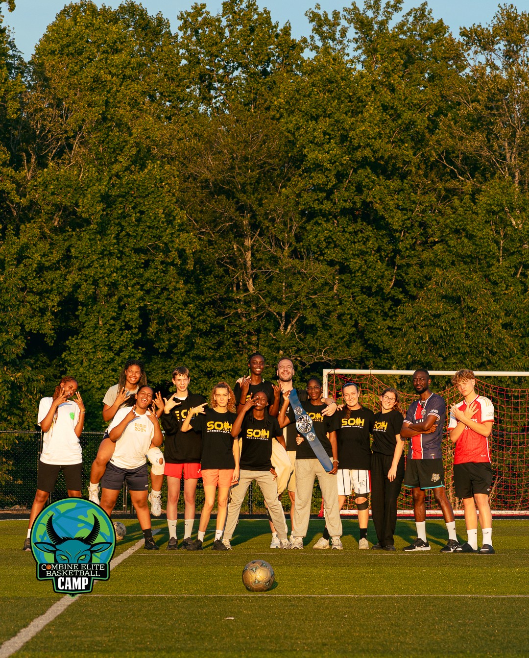 Groupe de jeunes participants d’un camp sportif posant devant un but de foot en extérieur.
